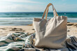 Blank white cotton tote bag shopper mock-up on sandy beach, clear blue sea and sky in the background. For eco friendly branding and summer promotions