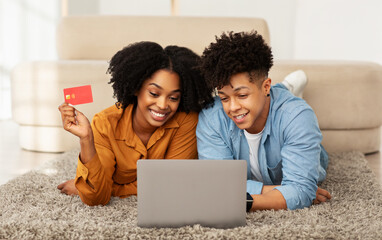 Wall Mural - A cheerful young couple is engaged in online shopping, with the woman holding a credit card