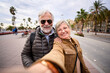 © CarlosBarquero - Happy Caucasian senior tourist couple take selfie together. Husband and wife love smiling looking at camera enjoying pensioner journeys in European city street. Older people retirees sightseeing
