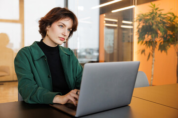 Focused DevOps Engineer, a woman, reads data on her computer screen in a modern office, collaborating with data science and financial analysts. Female jobs in demand for the young generation