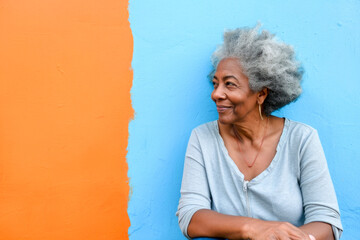 Wall Mural - Afroamerican famele with grey hair and in casual outfit against blue and orange wall