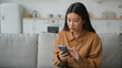 © Yuliia - Sad disappointed upset woman Asian chinese japanese girl lady in kitchen reading bad news in chat app on mobile phone failure connection mistake trouble rejected email lost message smartphone problem