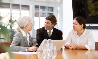 Wall Mural - Adult man, elderly woman and young woman in business clothes having meeting in office