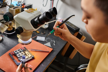 asian repairman testing micro schemes of electronic gadget near professional tools in workshop