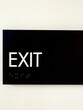 Black exit sign on a white wall with braille