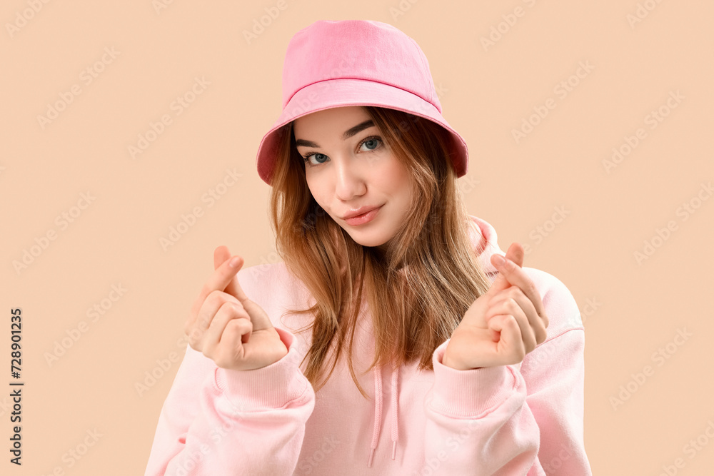 Young woman making heart with her fingers on beige background