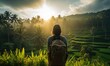 Enchanting Bali Sunrise: A Happy Tourist Woman, Back View, Admires the Breathtaking Sunrise Over Lush Green Rice Terraces. Palm Trees in the Distance Create a Scenic Vacation Memory.

