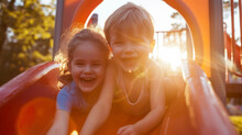 Two Siblings Playing Together On A Playground Their Faces Lit Up With Excitement As They Climb And Slide In The Suns Rays.