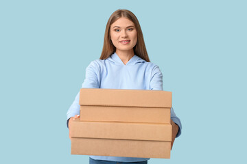 Sticker - Pretty young woman with cardboard boxes on blue background. Moving house concept