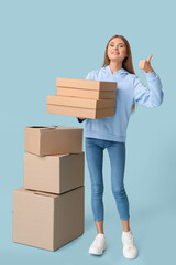 Sticker - Pretty young woman with cardboard boxes showing thumb-up on blue background. Moving house concept