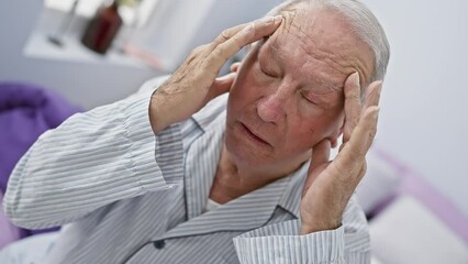 Wall Mural - Stressed senior man, sitting in bed, suffering migraine and pain in head. he's wearing pyjama, hand on head, face showing sadness. indoor portrait, intimate bedroom scene.