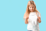 Fototapeta Na ścianę - Happy little girl with healthy teeth and paper tooth on blue background