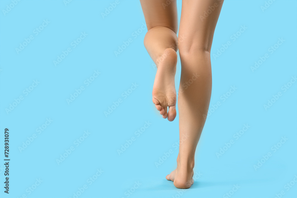 Barefoot woman walking on blue background, back view