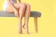 © Pixel-Shot - Barefoot woman sitting on soft bench against yellow background