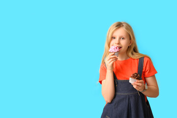 Wall Mural - Cute little girl eating cupcakes on blue background