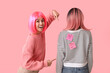 Beautiful young woman with paper stickers attached to her friend's back on pink background. April fools day celebration