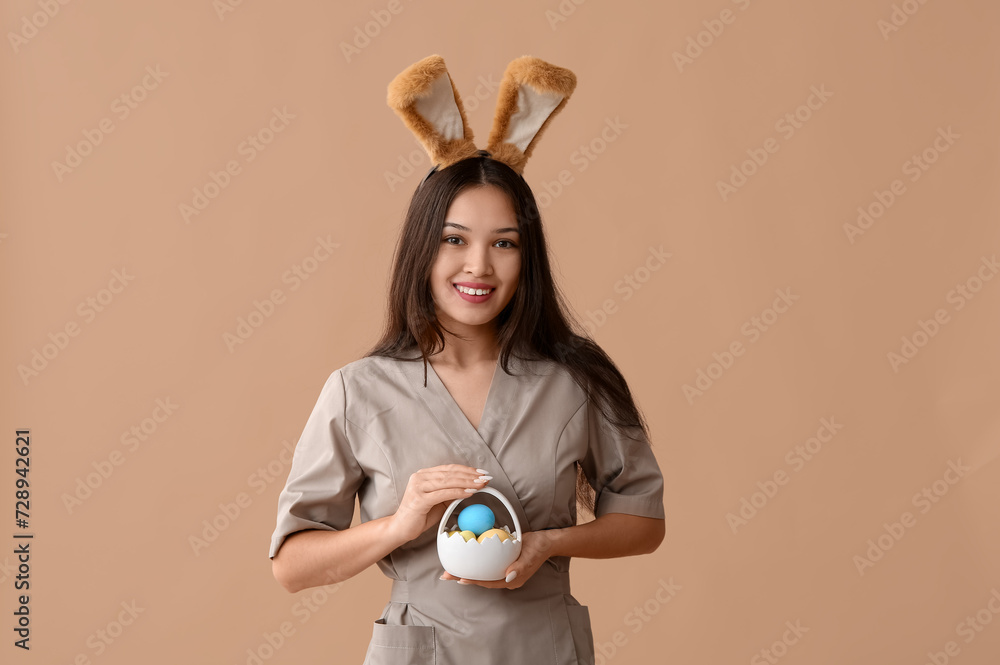 Female Asian massage therapist in bunny ears with Easter eggs on brown background