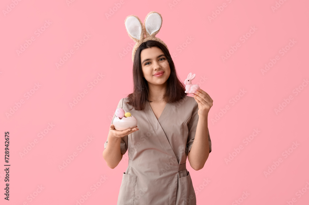 Female massage therapist in bunny ears with Easter rabbit and eggs on pink background