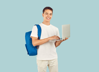 Happy clever tech high school coder student boy standing on light background uses laptop computer, prepares class project presentation, reads up for course test, browses information for academic essay