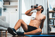 Athletic and sporty man drinking water on fitness mat after finishing home body workout exercise session for fit physique and healthy sport lifestyle at home. Gaiety home exercise workout training.
