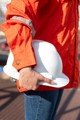 Wall Mural - An engineer or construction worker is holding a white safety helmet, wearing orange coverall, standing on the working platform walkway. Ready to work in the challenge workplace concept scene. 