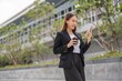 © StockPhotoRepublic - Young Asian Woman holding coffee cup and using phone outdoor in a central business district area