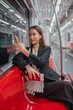© StockPhotoRepublic - Asian businesswoman with luggage using phone while taking a public skytrain transport to the airport