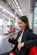© StockPhotoRepublic - Asian businesswoman with luggage using phone while taking a public skytrain transport to the airport