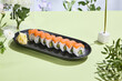 Artistic sushi composition with Philadelphia roll featuring salmon, avocado, and cheese in a floral summer setting
