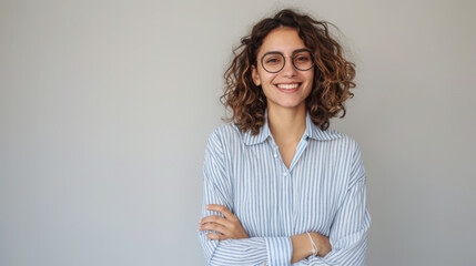 Wall Mural - woman with short blonde hair and a confident smile is wearing a white shirt and stands with her arms crossed against a light grey background