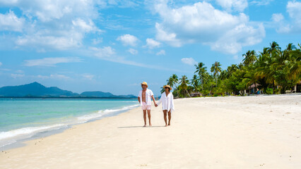 Wall Mural - Koh Mook a young couple of caucasian men and Thai Asian woman walking at the beach in Thailand