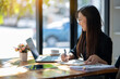 © Wasana - Attentive businesswoman jotting down notes while working on a project with her laptop at a sunny table..