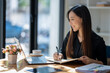 © Wasana - Attentive businesswoman jotting down notes while working on a project with her laptop at a sunny table..