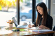 © Wasana - Attentive businesswoman jotting down notes while working on a project with her laptop at a sunny table..