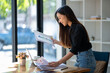 © Wasana - Cheerful businesswoman reviewing a financial report next to her laptop in a well-lit office space..