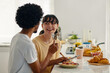© DragonImages - Young cheerful woman looking at her husband or boyfriend holding fork with tiny piece of homemade pizza by her mouth during breakfast