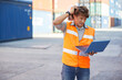 factory worker or engineer holding laptop computer and scratch his head when seeing a difficult situation at work in containers warehouse storage