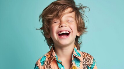 Wall Mural - A young boy with curly hair laughing joyfully with his eyes closed wearing a vibrant tropical-print shirt against a light blue background.