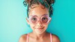 © iuricazac - A young girl with a joyful expression wearing pink goggles with water droplets on her face set against a vibrant blue background.