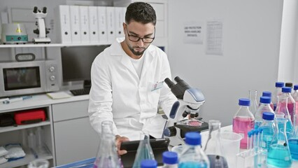 Sticker - A focused man in lab coat scrutinizes samples using a microscope in a modern laboratory setting.