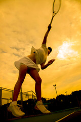 Wall Mural - silhouette of a female tennis player making a tennis serve against the backdrop of the sunset sky