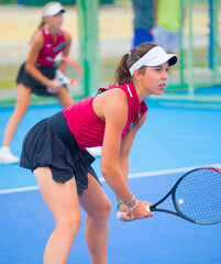 Wall Mural - A girl plays tennis on a court with a hard blue surface on a summer sunny da