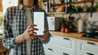 © Girts - Woman in Kitchen Holding Phone with Blank Screen. Over-the-Shoulder View. Engrossed in Cooking Preparation. Smart Home System Awaits Her Commands