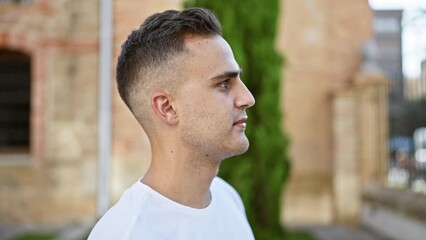 Wall Mural - Profile of a handsome hispanic man in casual attire outdoors with blurred urban background.