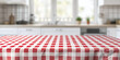 an empty table with a red and white checkered tablecloth on a blurred background of a light kitchen