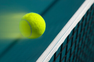 A tennis ball flies over a tennis net at high speed and leaves a trail behind it.