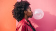 beautiful African-American woman blowing a bubble of bubble gum against a coloured wall