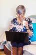 © Austockphoto - senior woman working on laptop on lounge with a cup of tea