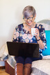 © Austockphoto - senior woman working on laptop on lounge with a cup of tea