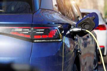 Close-up modern electric plug-in hybrid car parked near fast charger charging station point in center street old European city. Eco friendly green energy vehicle. Zero emission transport technology